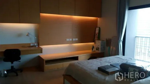 公寓 出租在Watthana, Bangkok - 卧室内置书桌与储物柜，暖色灯带，临近阳台。