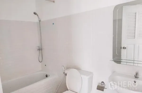 Townhouse for rent in Chatuchak, Bangkok - Bathroom with bathtub, toilet, sink, and wall mirror in white tiles.
