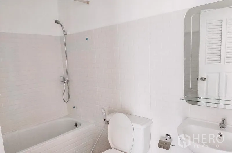 Townhouse for rent in Chatuchak, Bangkok - Bathroom with bathtub, toilet, sink, and wall mirror in white tiles.