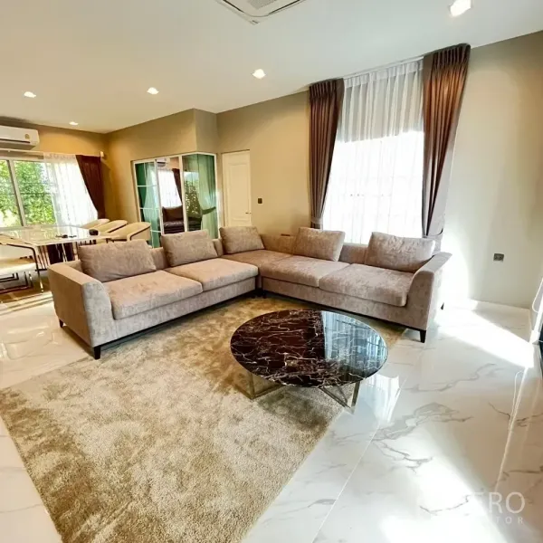 Detached House for rent or sale in Bang Khen, Bangkok - Bright living room with L‑shaped sofa, marble coffee table and large windows.