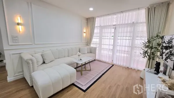 独立式住宅 出租在Huai Khwang, Bangkok - 曼谷辉煌区独栋别墅的明亮客厅，白色L形沙发、木地板与纱帘。
