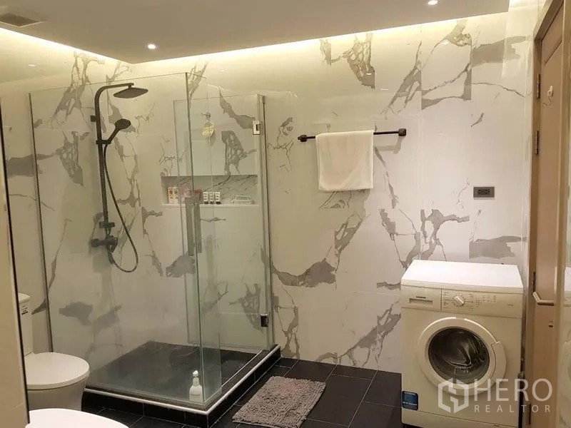 Condominium for rent in Bang Rak, Bangkok - Marble-tiled bathroom with glass shower enclosure, rain shower and a washing machine.