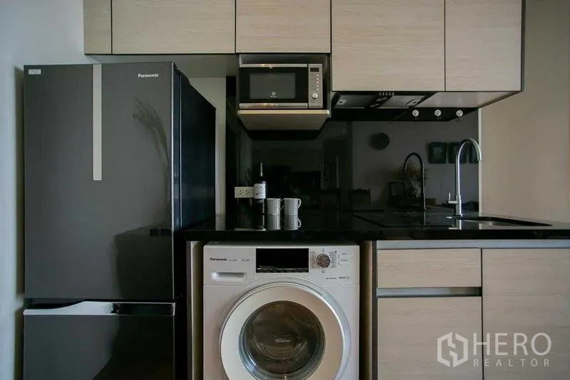 Condominium for sale in Khlong Toei, Bangkok - Appliance wall with refrigerator, microwave, and front-load washer under cabinets.