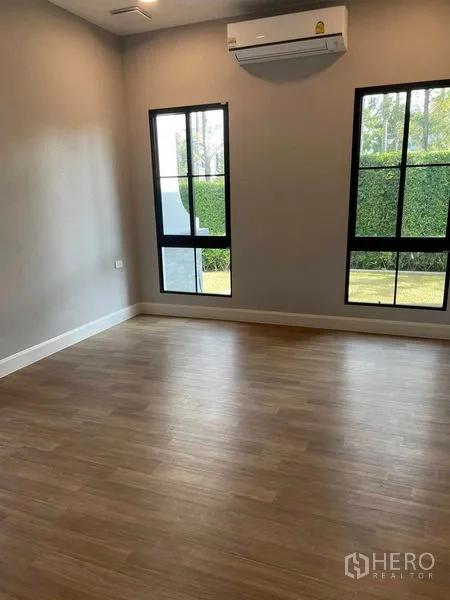 Detached House for sale in Saphan Sung, Bangkok - Ground‑floor bedroom with twin tall windows and wood flooring.