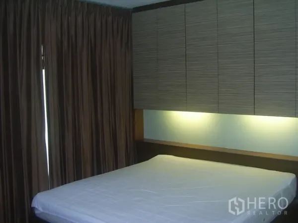Condominium for rent in Khlong Toei, Bangkok - Bedroom with overhead cabinets, soft headboard lighting, and floor-to-ceiling drapes.