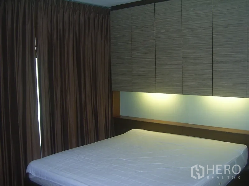 Condominium for rent in Khlong Toei, Bangkok - Bedroom with overhead cabinets, soft headboard lighting, and floor-to-ceiling drapes.