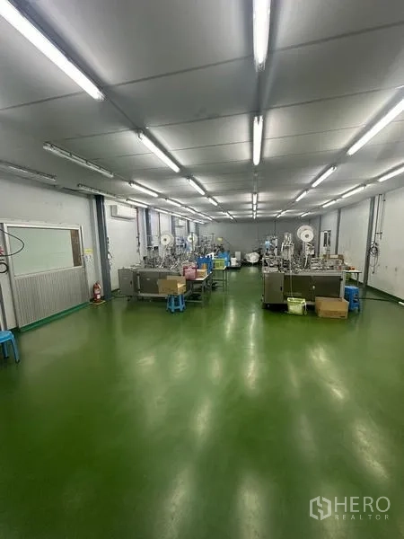 Warehouse for rent or sale in Lam Luk Ka, Pathum Thani - Production floor with machinery lines under bright fluorescent lighting.