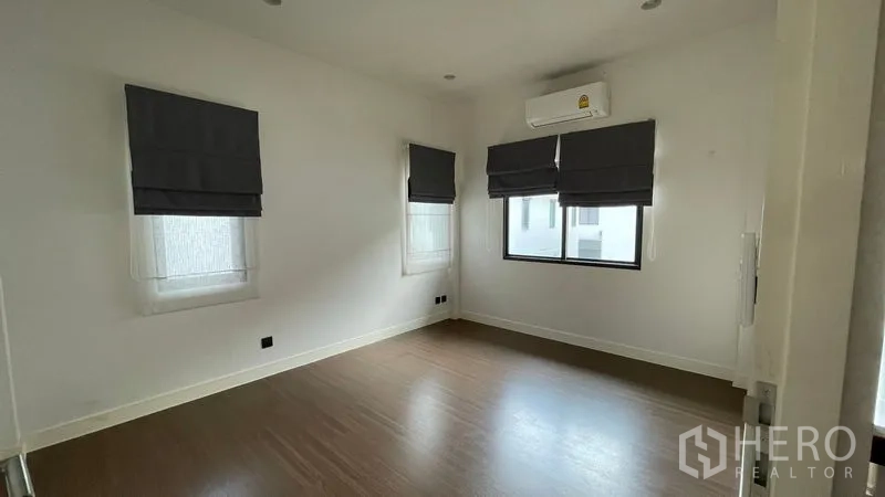 Detached House for rent in Bang Kapi, Bangkok - Empty bedroom with wood flooring, air conditioner and three windows with Roman blinds.