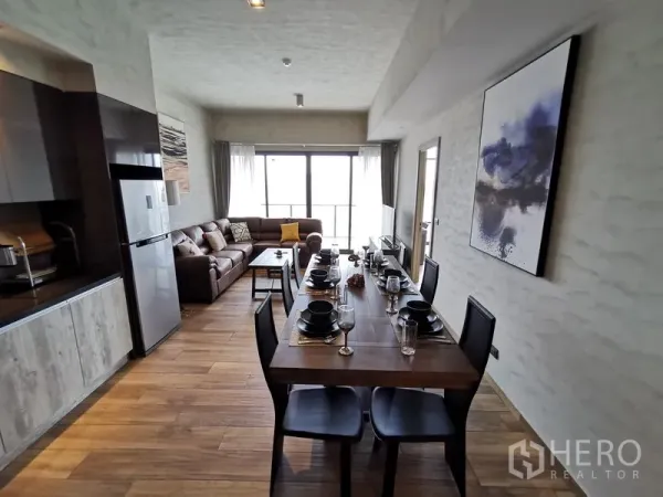 公寓 出租在Watthana, Bangkok - 开放式厨房连接六人餐桌，通向带大沙发的起居区，正对宽幅落地窗。