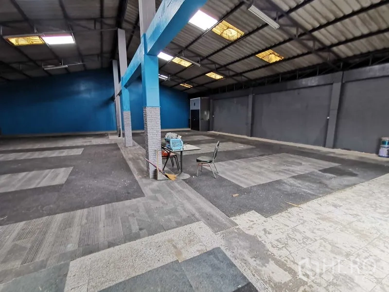 Warehouse for rent in Nonthaburi - Open warehouse floor with blue columns and gray walls, small table and chair in the center.
