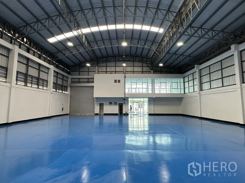 Factory for rent in Khlong Luang, Pathum Thani - Spacious production hall with high arched steel roof, skylights and glossy blue epoxy flooring.