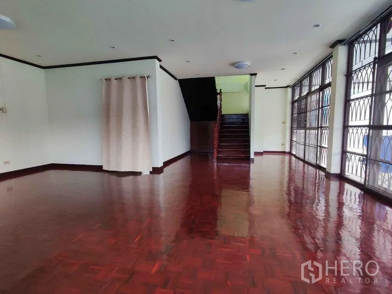 独立式住宅 出租在Khlong Toei, Bangkok - 一层开放式起居区，光亮木地板，楼梯与整面带护栏的窗户。