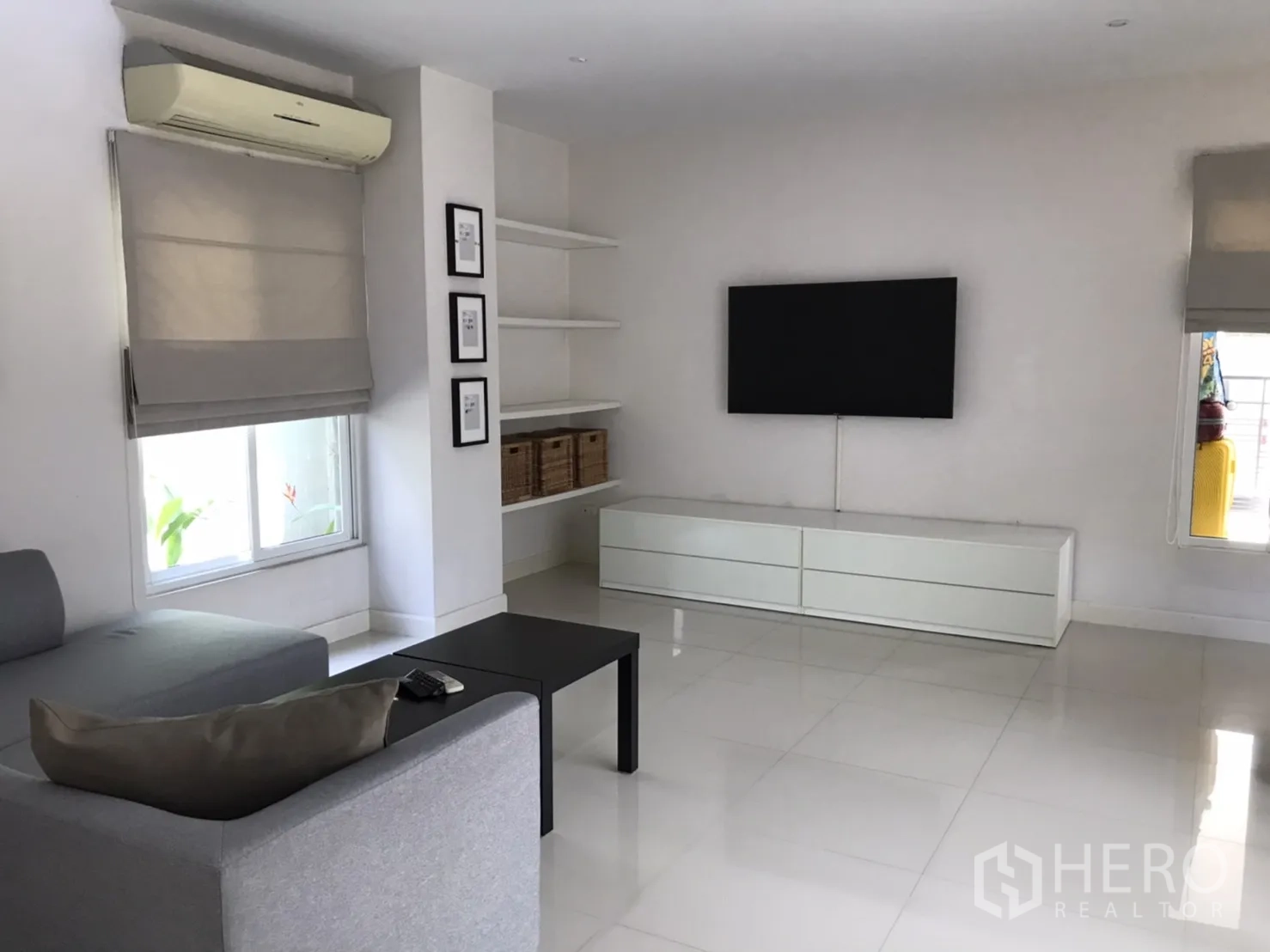 Detached House for rent or sale in Saphan Sung, Bangkok - TV lounge with wall-mounted screen, built-in shelves and large windows with blinds.