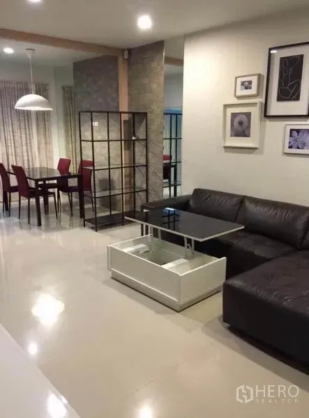 Townhouse for rent in Wang Thonglang, Bangkok - Open-plan living and dining area with a black leather sectional, lift-top coffee table, red dining chairs, and pendant lighting.