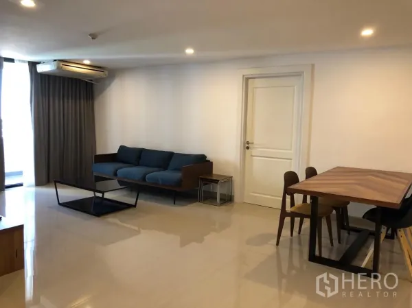 公寓 出租在Watthana, Bangkok - 宽敞客餐厅，蓝色沙发、木质餐桌、空调与落地窗帘