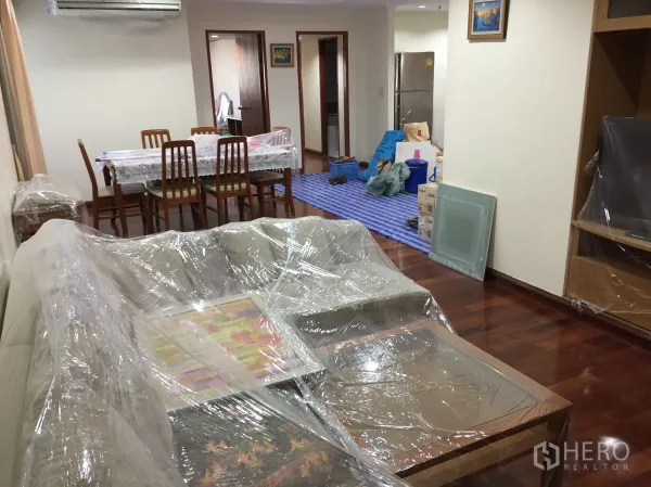 Condominium for rent in Watthana, Bangkok - Spacious lounge and dining area with sofa set, six-seat dining table, air conditioner, and a kitchen zone at the far end.