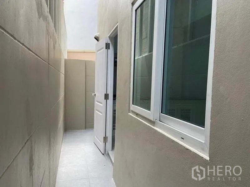 Townhouse for rent in Bang Na, Bangkok - Tiled side service yard with exterior windows and a white door.