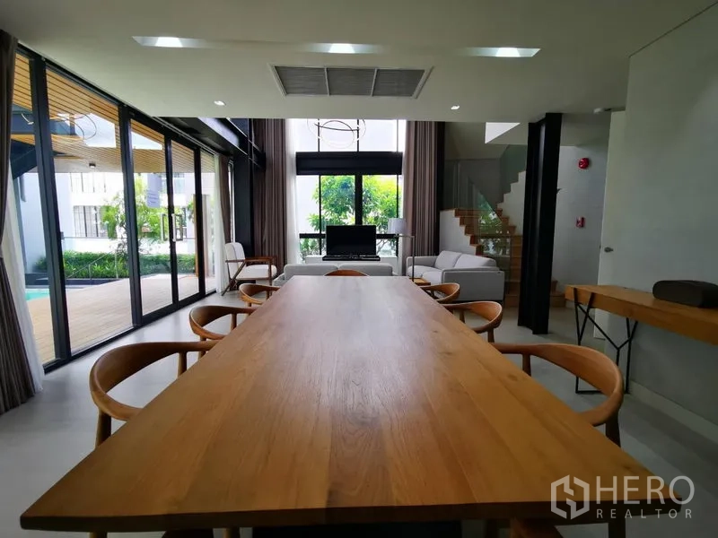 Apartment for rent in Khlong Toei, Bangkok - Open-plan dining and living area with a long wooden table, floor-to-ceiling windows, and views to the poolside deck.