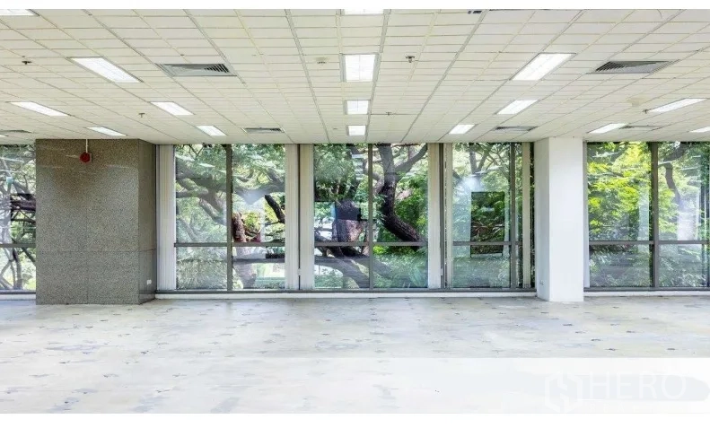Office Space for rent in Pathum Wan, Bangkok - Bright unfurnished office with floor-to-ceiling windows overlooking lush trees and a grid ceiling with lights.