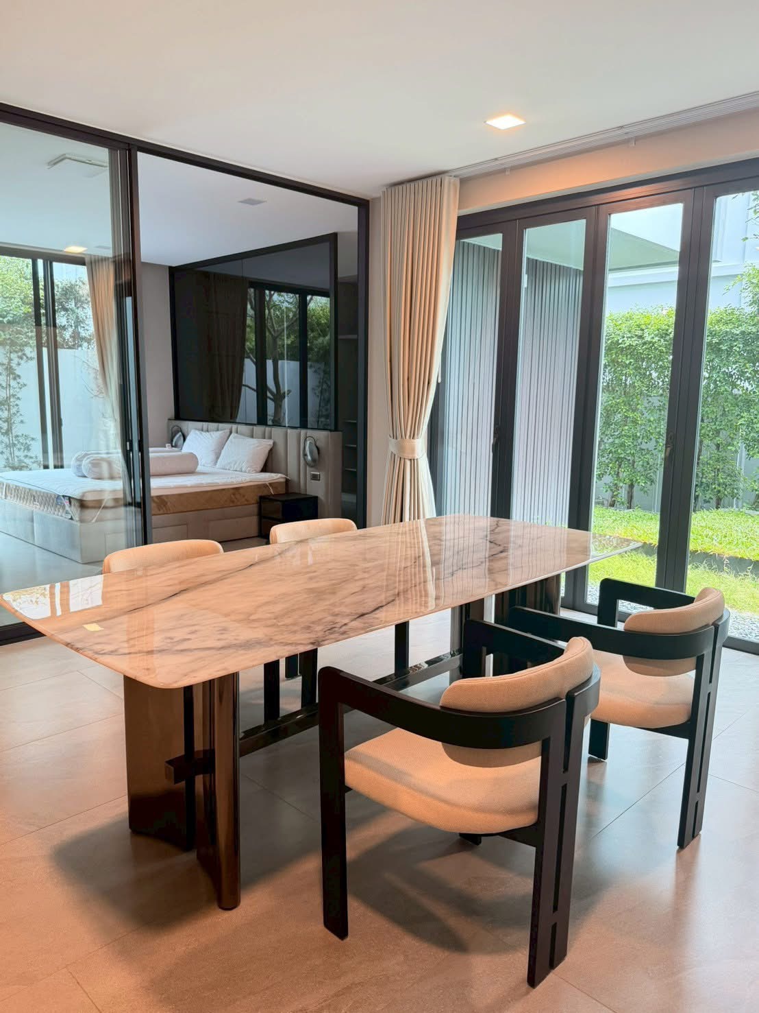 Detached House for rent in Saphan Sung, Bangkok - Contemporary dining area with a marble table, cushioned chairs and floor-to-ceiling glass overlooking a green garden.