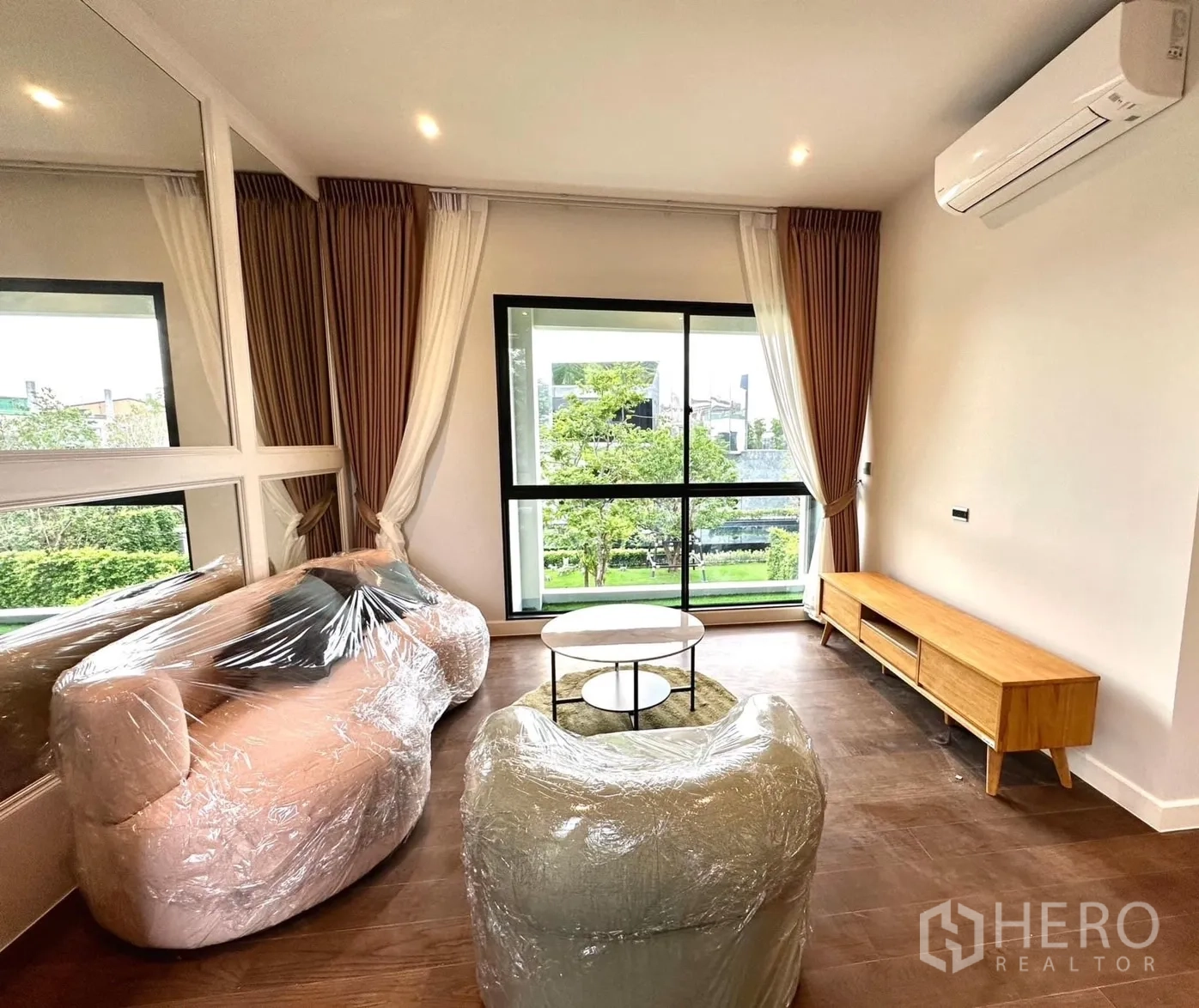 Detached House for rent - Bright family room with large windows, air conditioner, wrapped sofas and a wooden TV console overlooking greenery.