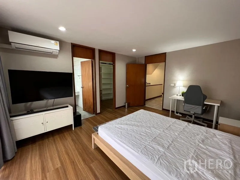 Townhouse for rent or sale in Suan Luang, Bangkok - Air-conditioned bedroom with bed, TV, work desk and en-suite access on warm wood floors.