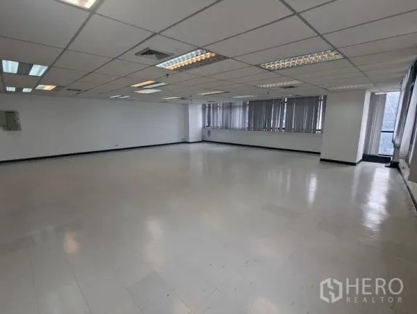 Office Space for rent or sale - Large empty office area with multiple ceiling light panels, AC vents, and wraparound windows providing natural light.
