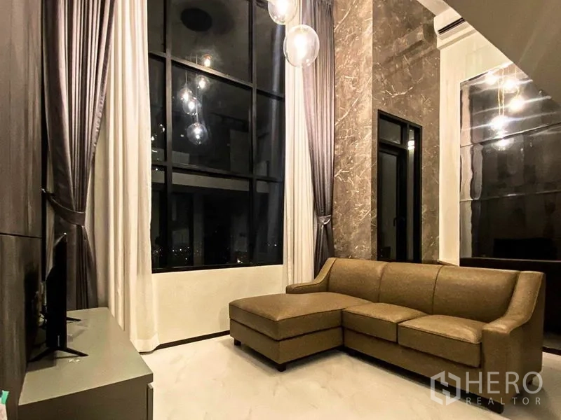 คอนโด ให้เช่าในSathon, Bangkok - ห้องนั่งเล่นเพดานสูง โซฟาเข้ามุม ผนังหินอ่อน และหน้าต่างแบบฟลอร์ทูซีลิงยามค่ำ
