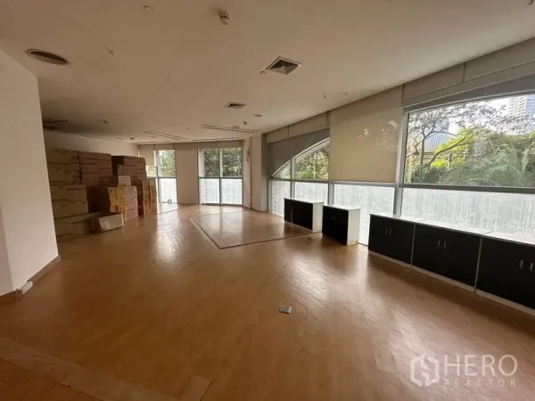 Office Space for rent in Pathum Wan, Bangkok - Large office with wood floors, built-in low cabinets, and tree views through wide windows.