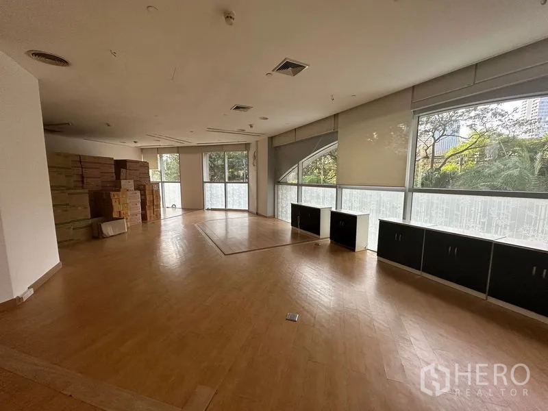 Office Space for rent in Pathum Wan, Bangkok - Large office with wood floors, built-in low cabinets, and tree views through wide windows.