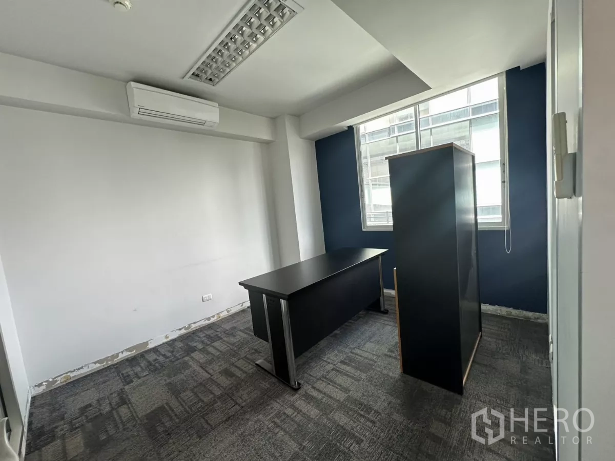 办公空间 出租在Watthana, Bangkok - 紧凑经理室，蓝色特色墙、地毯铺装，窗边自然采光。