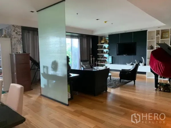 Condominium for sale in Khlong Toei, Bangkok - Open-plan living area with wood floors, TV wall, shelving and sliding glass to the balcony.