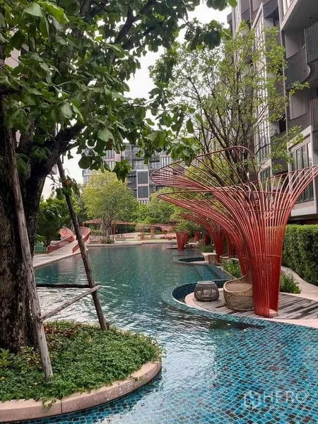 公寓 出售在Watthana, Bangkok - 度假风泳池，配红色雕塑遮阳装置与繁茂树木。