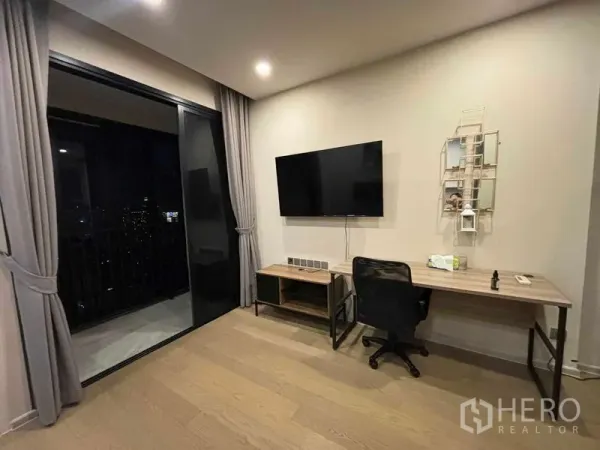 Condominium for rent in Watthana, Bangkok - Workspace with desk and TV beside floor-to-ceiling sliding door to a balcony with night view.