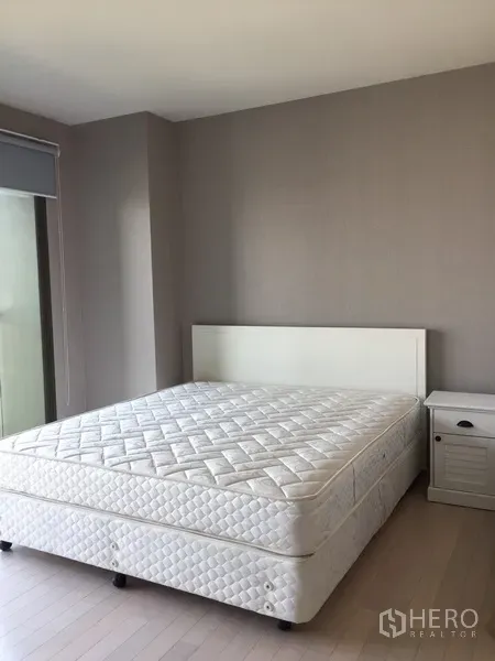 Condominium for rent in Watthana, Bangkok - Bright bedroom with white bed, bedside table and neutral walls in a Bangkok condominium.