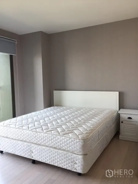 Condominium for rent in Watthana, Bangkok - Bright bedroom with white bed, bedside table and neutral walls in a Bangkok condominium.