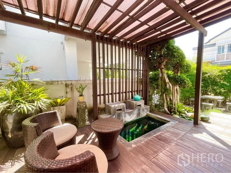 独立式住宅 出售在Prawet, Bangkok - 花园中的木质露台与凉棚，藤椅和小型景观水池。