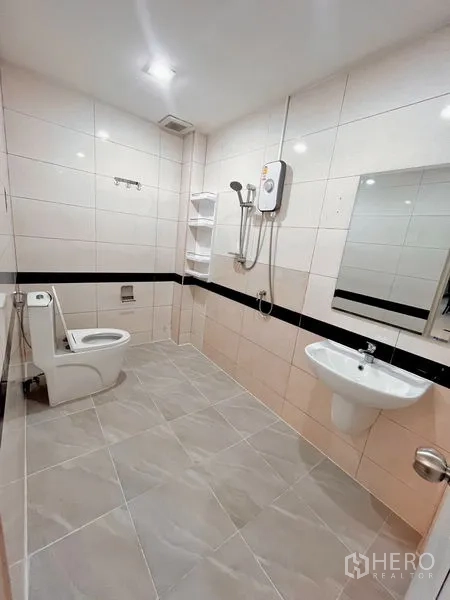 Townhouse for rent in Huai Khwang, Bangkok - Fully tiled bathroom with toilet, sink, mirror and shower heater.