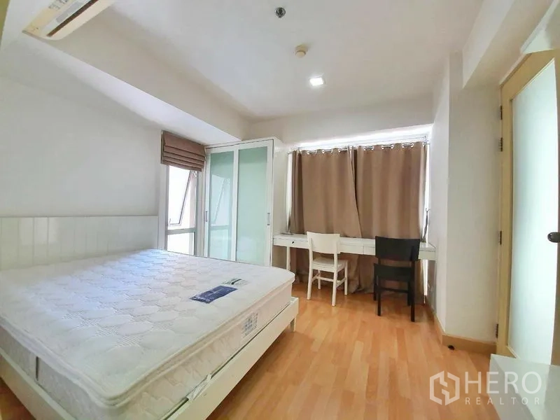 Condominium for rent in Din Daeng, Bangkok - Spacious bedroom with desk and chairs, wardrobe, wood flooring, and natural light from windows.