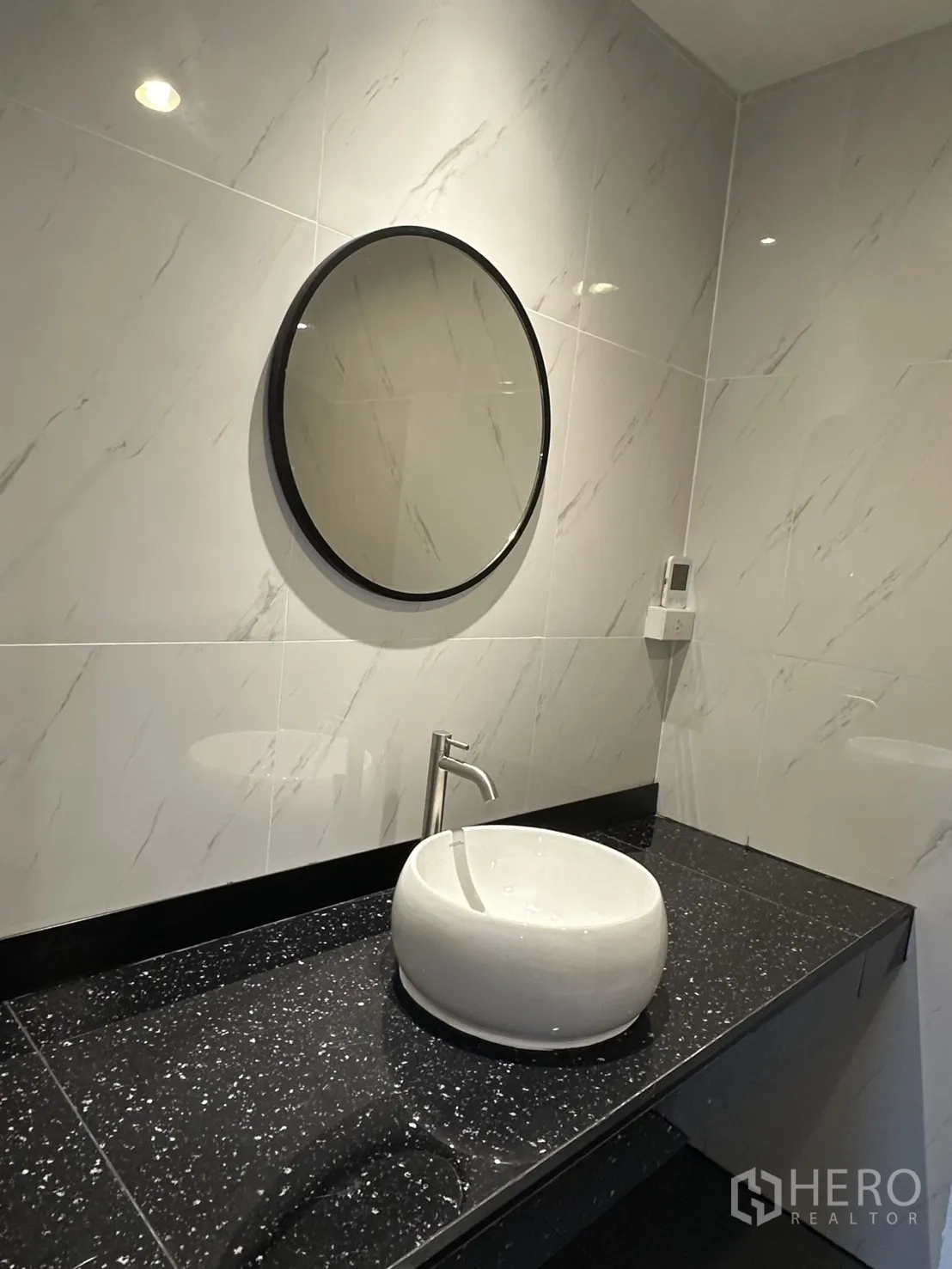 Home Office for rent in Khlong Toei, Bangkok - Bathroom vanity with round mirror and white vessel sink on a black countertop.