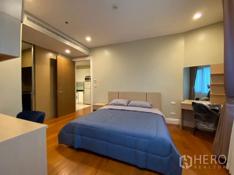 Condominium for rent in Khlong Toei, Bangkok - Primary bedroom with double bed, desk and warm wood flooring.