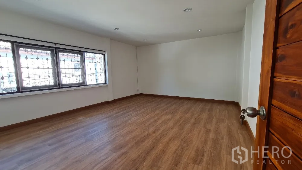 Detached House for rent in Lat Phrao, Bangkok - Spacious bedroom with wide windows and wood flooring.