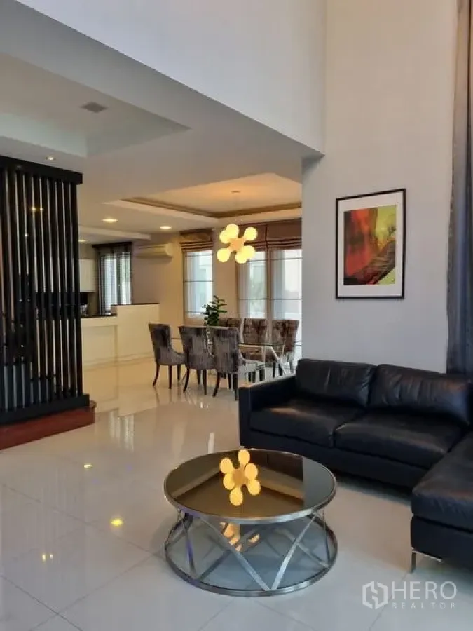 Detached House for sale in Chatuchak, Bangkok - Open-plan lounge leading to dining and kitchen, with black leather sofa and a round glass table.