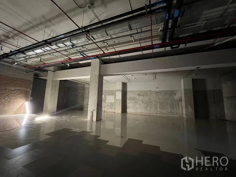 零售空间 出租 - 宽敞未完成零售楼层，裸露机电管线、混凝土柱与瓷砖地面。