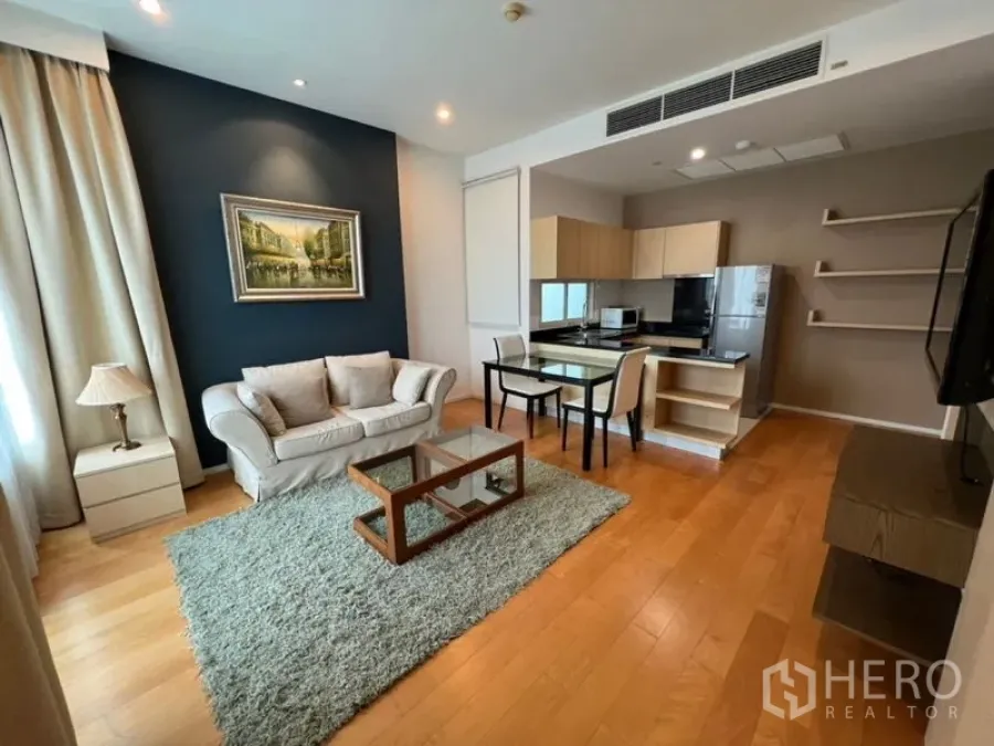 Condominium for rent in Chatuchak, Bangkok - Bright living room with sofa, glass coffee table, rug and open kitchen on wood floors