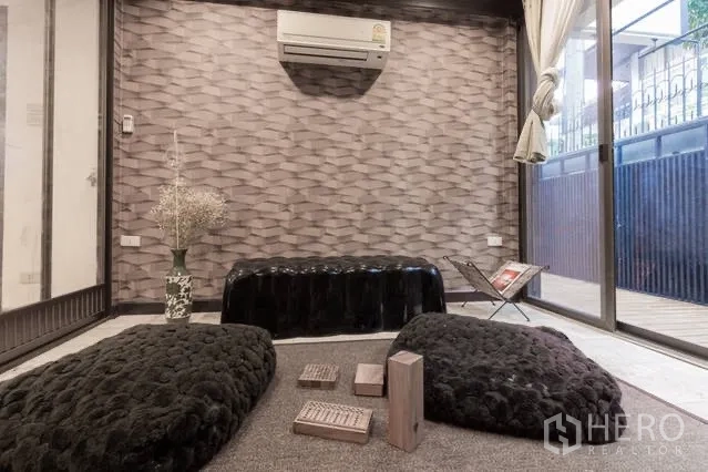 Detached House for rent in Watthana, Bangkok - Cozy sitting room with textured feature wall, floor cushions and large sliding glass doors.