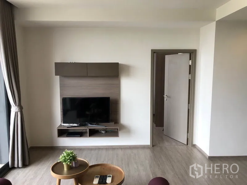 Condominium for rent in Watthana, Bangkok - Modern living area with mounted TV wall unit, light wood floors, and doorway to the bedroom.
