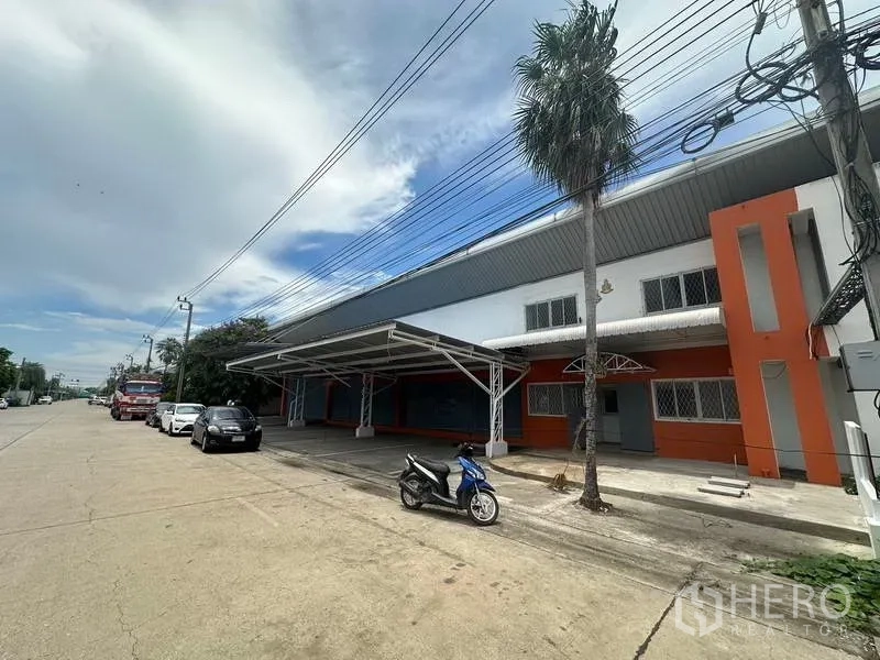 Factory for rent in Nonthaburi - Side frontage of the factory with covered bay, palm tree and easy truck access along the road.