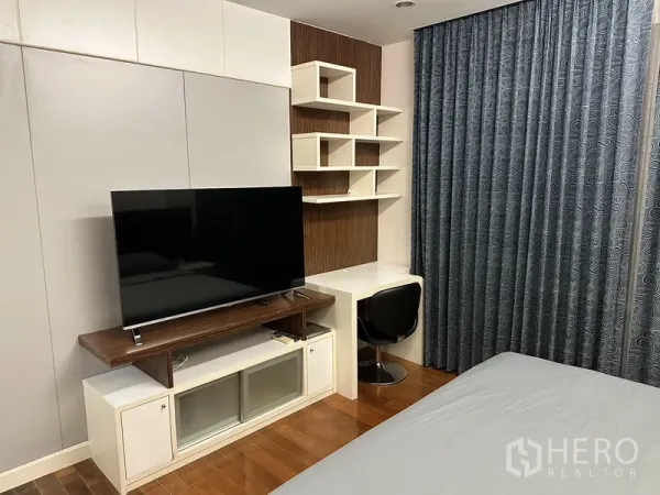 公寓 出租在Watthana, Bangkok - 卧室一角，电视柜与内置书桌及几何置物架，木地板与遮光窗帘。