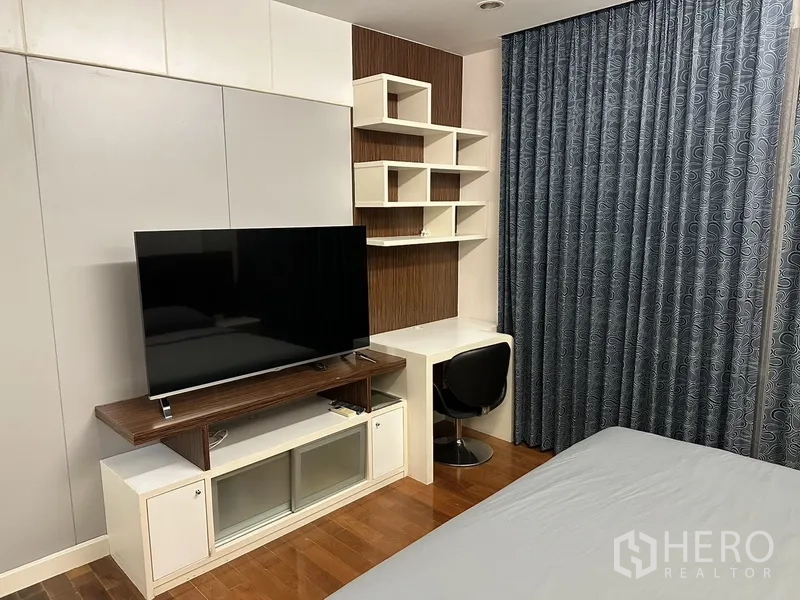 公寓 出租在Watthana, Bangkok - 卧室一角，电视柜与内置书桌及几何置物架，木地板与遮光窗帘。
